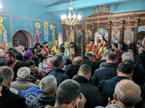 People worshipping in an Eastern Orthodox church. Several priests lead the service in ornate robes.