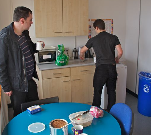 Two men in an office kitchen making coffee and tea