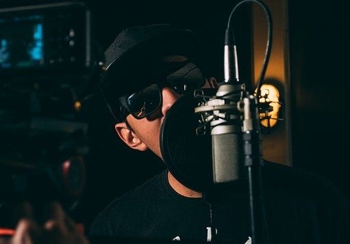 Image of a man in sunglasses rapping into a microphone.