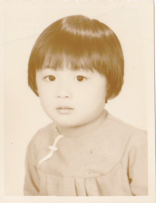 An old black and white photo of an Asian child, with black hair, wearing a dress with a collar.