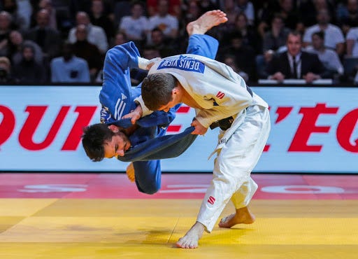 A man in the process of taking down his opponent to the ground in a Judo competition