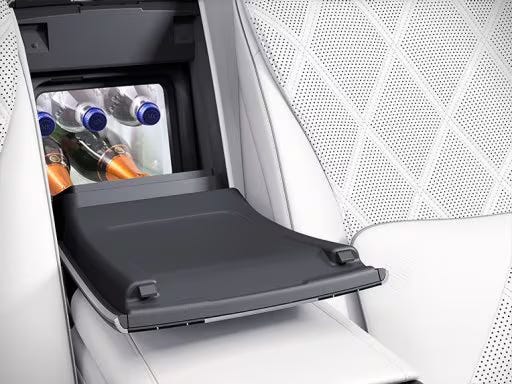 A built-in car refrigerator located between white leather seats, containing bottles and cans, showcasing a luxury feature for convenience and storage.