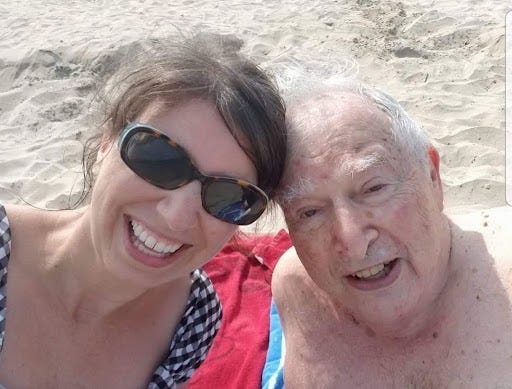 A white woman and her elderly father smiling at the beach.