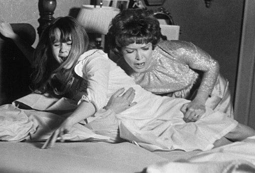 A photo from the horror film, The Exorcist where Linda Blair’s mother is trying to help her devil possessed daughter.