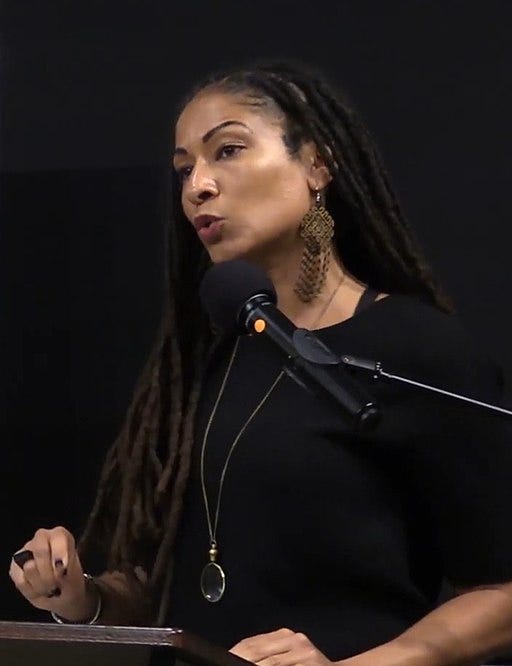 person with long hair and earrings speaking into a microphone