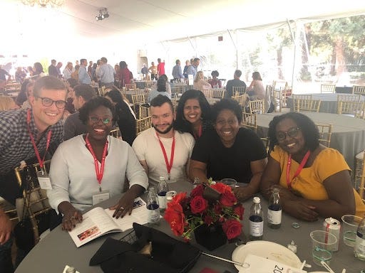 Diverse group of Stanford Law alums sitting at a table adorned with red flowers at a Stanford Law Reunion event