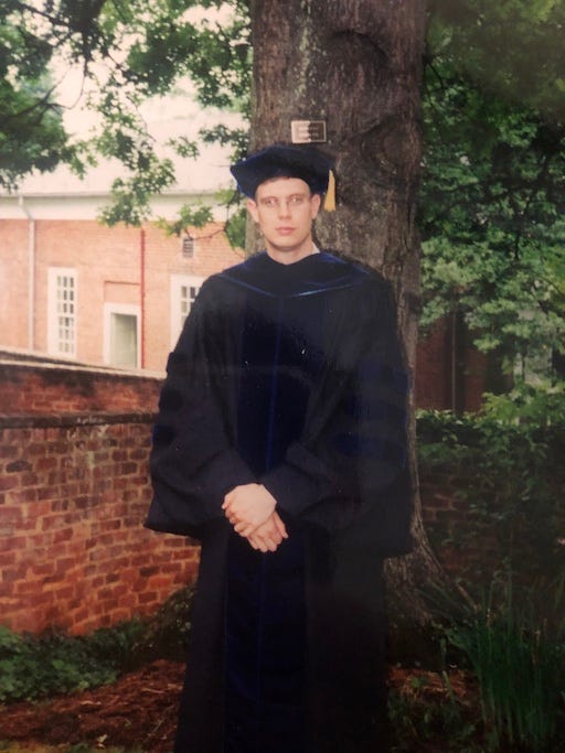 Photo of the author, age 29, wearing cap, gown, and PhD hood, standing in a garden at the University of Virginia on graduation day, 2001.