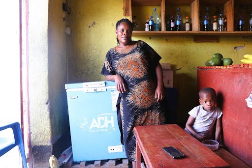 A woman leans on her refrigerator chest as her young son sits in a nearby bench in the restaurant she owns.