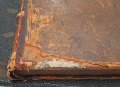 Close up of the lower spine left hand corner of a book covered in leather which has red rot. The leather has deteriorated, is red and powdering and has suffered losses across the edge of the front board.