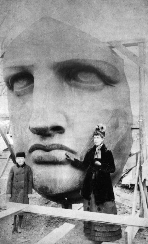 Black and white photo of the copper face of Liberty, uncrated, and viewed by tourists