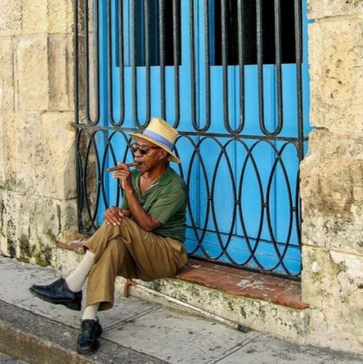 Cuban man smokes cigar on a step in front of a distinctive sky blue doorway