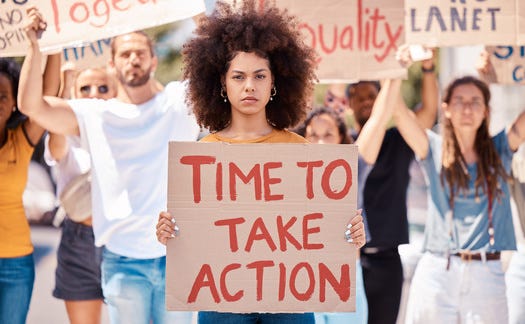 Image of a lady with brown afro hair holding a sign with the words ‘Time to Take Action’ written on it in red.