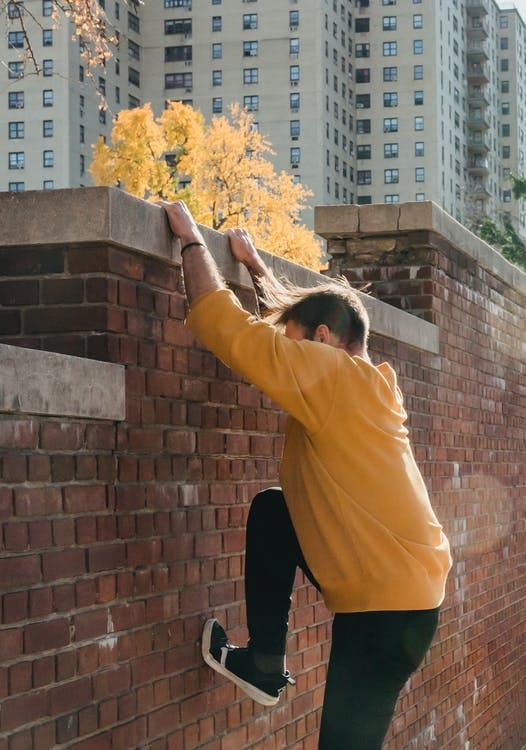 Faceless man in yellow about to climb over a red brick wall in autumn, passing obstacles photography