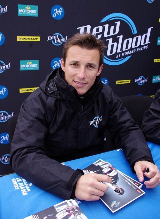 Christian Klien, wearing a black team jacket, at an autograph signing at Le Mans with a not quite cheesy grin.