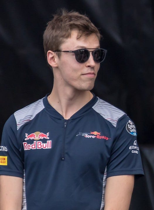 Daniil Kvyat wearing the Torro Rosso uniform and sunglasses, grinning slightly at someone out of frame.