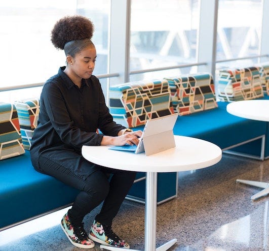 A Black woman with an afro wearing all black works on her laptop.
