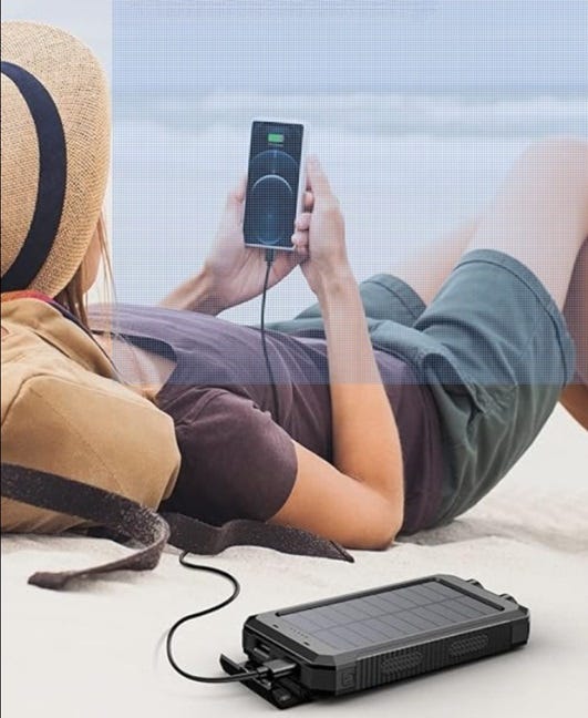 Woman relaxing on the beach using her cell phone to listen to music and it is plugged into a portable backup power charging device.