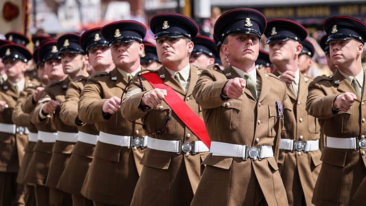 British Army soldiers dressed in ceromonial uniforms march in line down the street as part of the event.