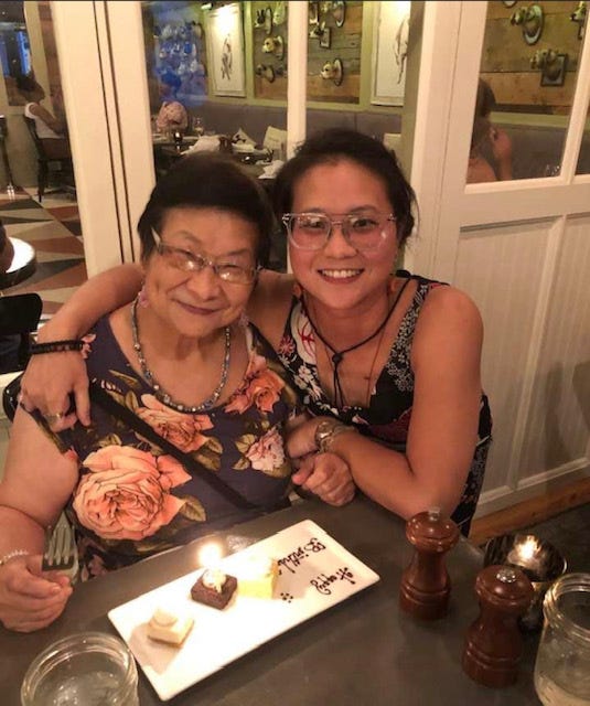 An Asian mother and daughter smile for a picture with a slice of cake at a birthday gathering in a restaurant.