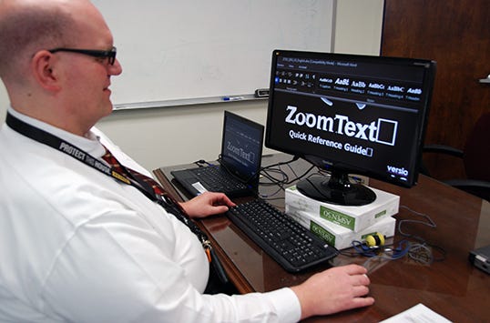A person in white shirt using a computer with zoomed text on the screen