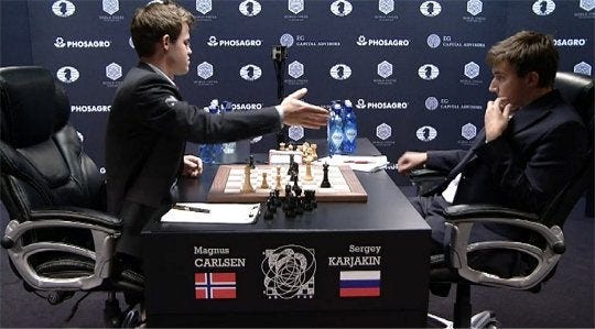 Imagem do Match Carlsen x Karjakin, disputado em 2016 valendo o título de Campeão Mundial de Xadrez. Na imagem, Magnus Carlsen, à esquerda, estende a mão para abandonar a oitava partida do match. Os jogadores estão de perfil, sentados em frente ao tabuleiro com a posição final da oitava partida.