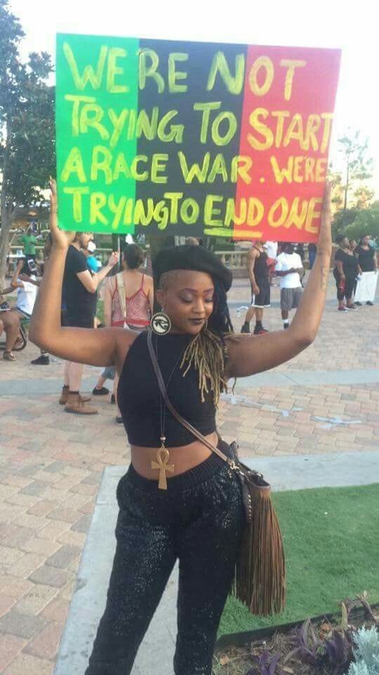 A Black person holding a colourful sign saying“We’re not trying to start a race war we’re trying to end one”