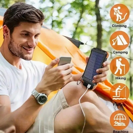 Smiling man sitting in front of his tent while camping and looking at his smartphone that is connected to a back-up battery pack portable charger.