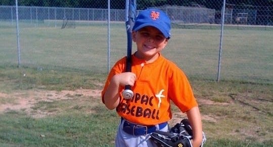 A photo of the author’s son holding a bat on his shoulder, a glove on his other hand and donning a New York Mets hat on his head. Smiling proudly.