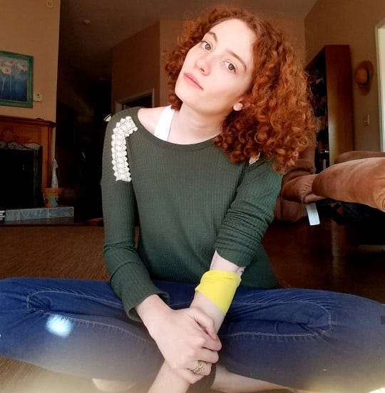 Photo of the author wearing regular clothes with clean hair and makeup, sitting cross legged and looking at the camera.