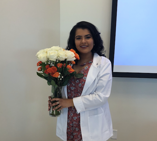 Juhi wearing a white coat holding a vase of flowers.