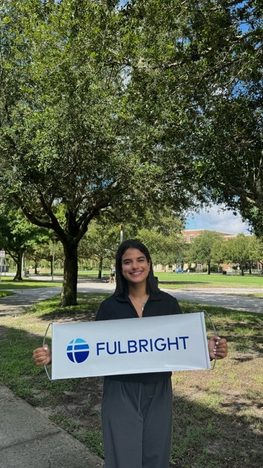 Sarah standing outside, wearing black, holding a Fulbright sign.