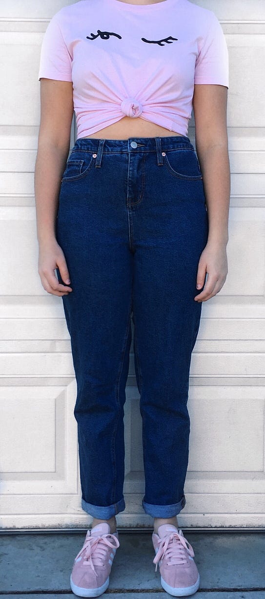 Dark blue high-waisted mom jeans worn with a pink graphic t-shirt and pink Adidas sneakers.