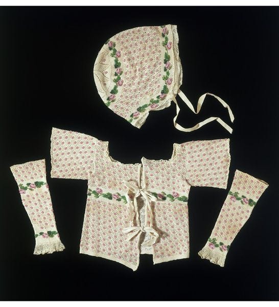 Set of hand knitted woollen baby clothes, English, 1800–1849. A matching set of baby clothes consisting of a cap, jacket and a pair of sleeves. The overall pattern is of openwork knitting decorated with clusters of pink beads. There are additional bands of plain knitting embellished with rose motifs made of pink and green glass beads. The cap and jacket have tapes attached to secure the clothes to the baby. Hand knitted wool.