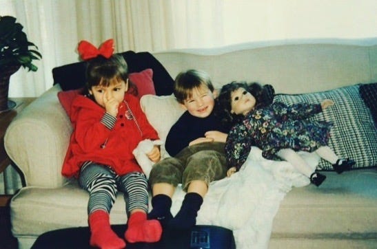 little girl and boy on a couch next to a large doll