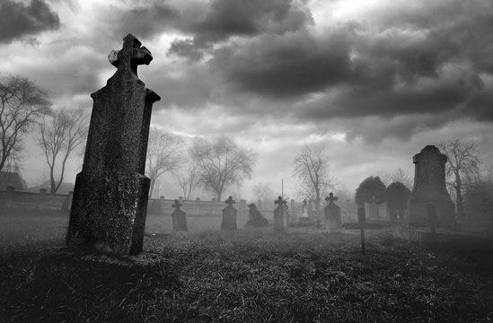 Black and white graveyard scene with headstones. Cloudy sky.