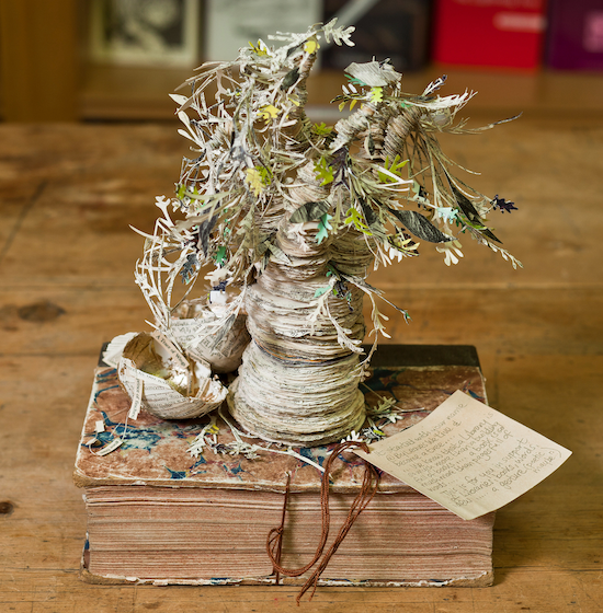 a tree that is crafted out of the pages of a book, shown in a photograph on top of an older book