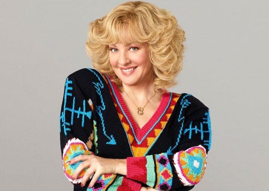 Beverly Goldberg wearing a black v-neck sweater with pink, blue, orange, yellow, and green patterns.