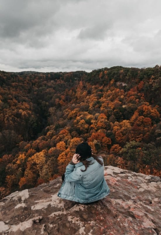 woman at the top of a mountain peak gazing out over foliage