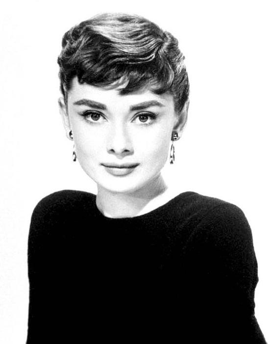 Black and white headshot of actress Audrey Hepburn. She is wearing a black sweater and looking straight at the camera.