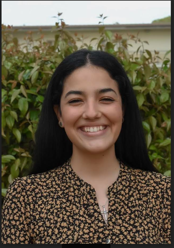 Photo of Cassandra Avila, smiling at the camera in front of a leafy bush.