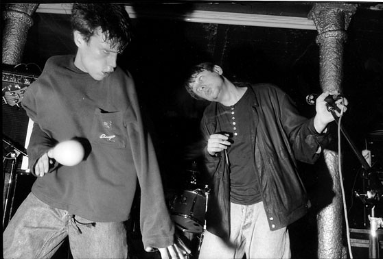 A black-and-white photo of 2 boys, who appear disorientated, each holding some kind of musical instrument.