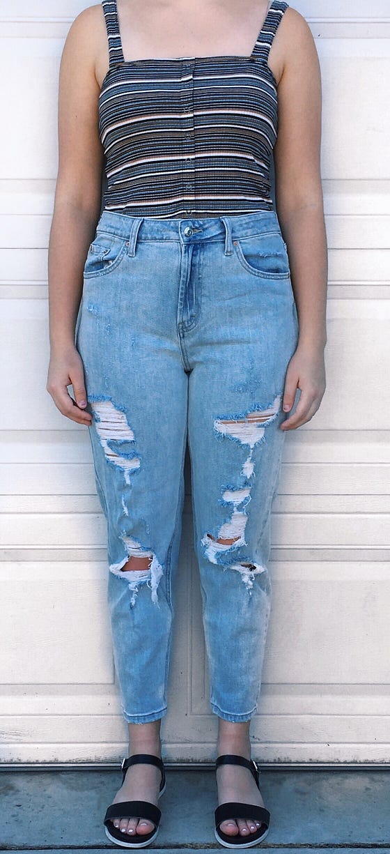 Ripped high-waisted mom jeans worn with a black striped semi cropped tank top and black and white sandals.