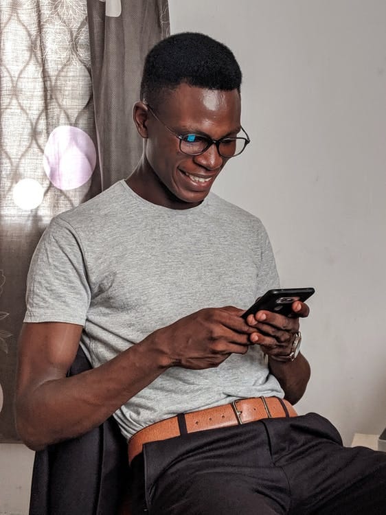 Man wearing glasses, sat down, looking at a smartphone