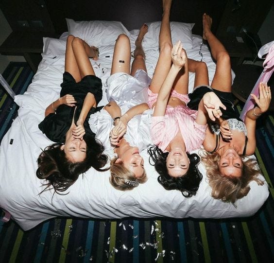 A bunch of teen girls laying on a bed chatting and laughing