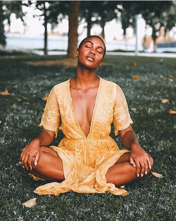 Black girl sitting in park, meditating in seated yoga position