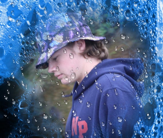 Teen boy wearing a hat behind a rainy window