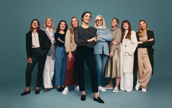 Nine women standing in a line facing the camera, all smiling and dressed in business clothing.