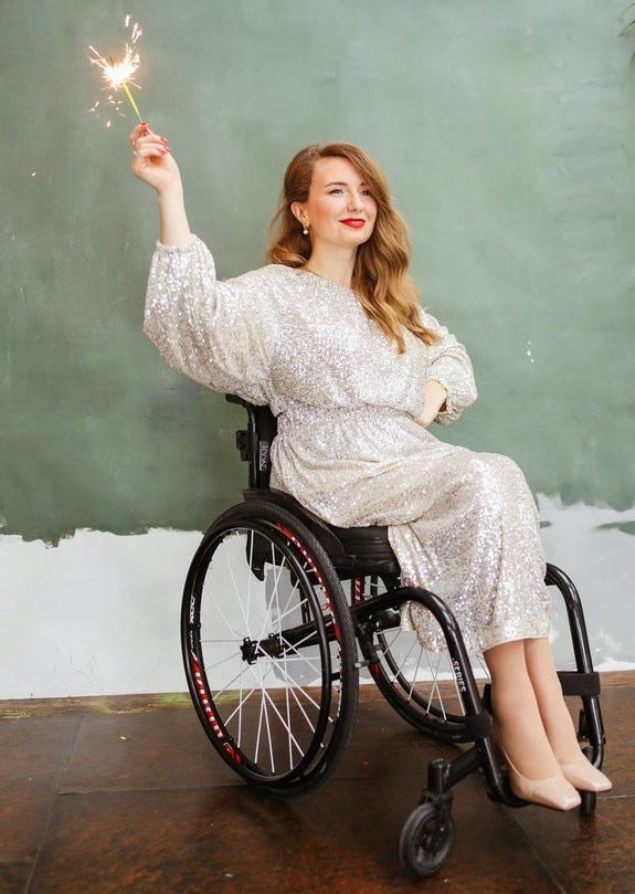 A person in a weelchair, wearing a sparkly sequins dress, and holding up a sparkler. Credit: Polina Tankilevich via Pexels