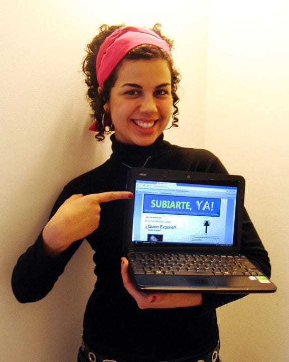 Luisa aos 26 anos mostrando em seu notebook o site da galeria de arte virtual latino americana, SUBIARTE, YA!