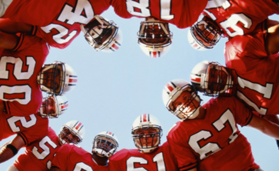 A group of angry football players standing in a circle facing the camera which is in the middle